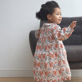 A child wearing the Pigeon Organics squirrel smock dress standing on a wooden surface showing the curved Peter Pan style collar and elasticated waist band detail