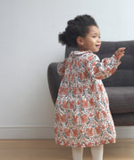 A child wearing the Pigeon Organics squirrel smock dress standing on a wooden surface showing the curved Peter Pan style collar and elasticated waist band detail