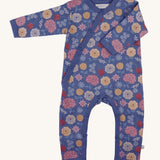 Pigeon Organics kimono romper. A 100% GOTS organic cotton in navy blue with long sleeves and popper fasteners at the front and between the legs. Features a print of multicoloured artistic flowers all over the garment. 
