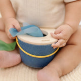 Close up of a baby's hand taking a blue cloth out from the PlanToys baby tissue box wooden sensory toy.
