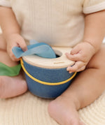 Close up of a baby's hand taking a blue cloth out from the PlanToys baby tissue box wooden sensory toy.