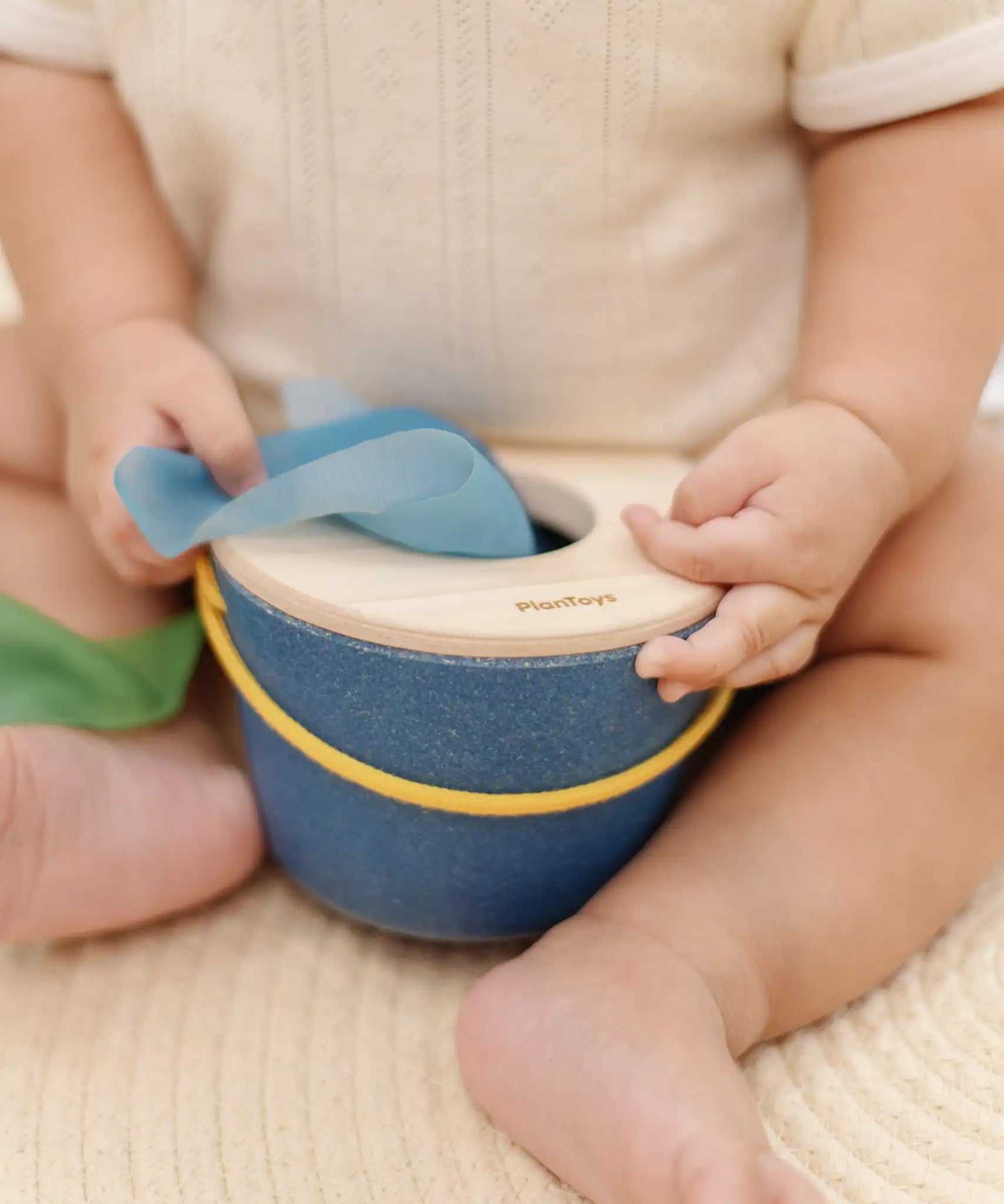Close up of a baby's hand taking a blue cloth out from the PlanToys baby tissue box wooden sensory toy.