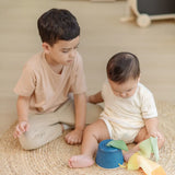 Baby pulling materials out of the PlanToys baby tissue box wooden sensory toy with an older sibling sitting besides them.