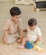 Baby pulling materials out of the PlanToys baby tissue box wooden sensory toy with an older sibling sitting besides them.
