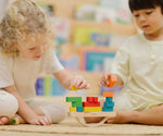 Children playing with the PlanToys balancing cargo wooden balance game. Stacking wooden blocks on the base piece. 