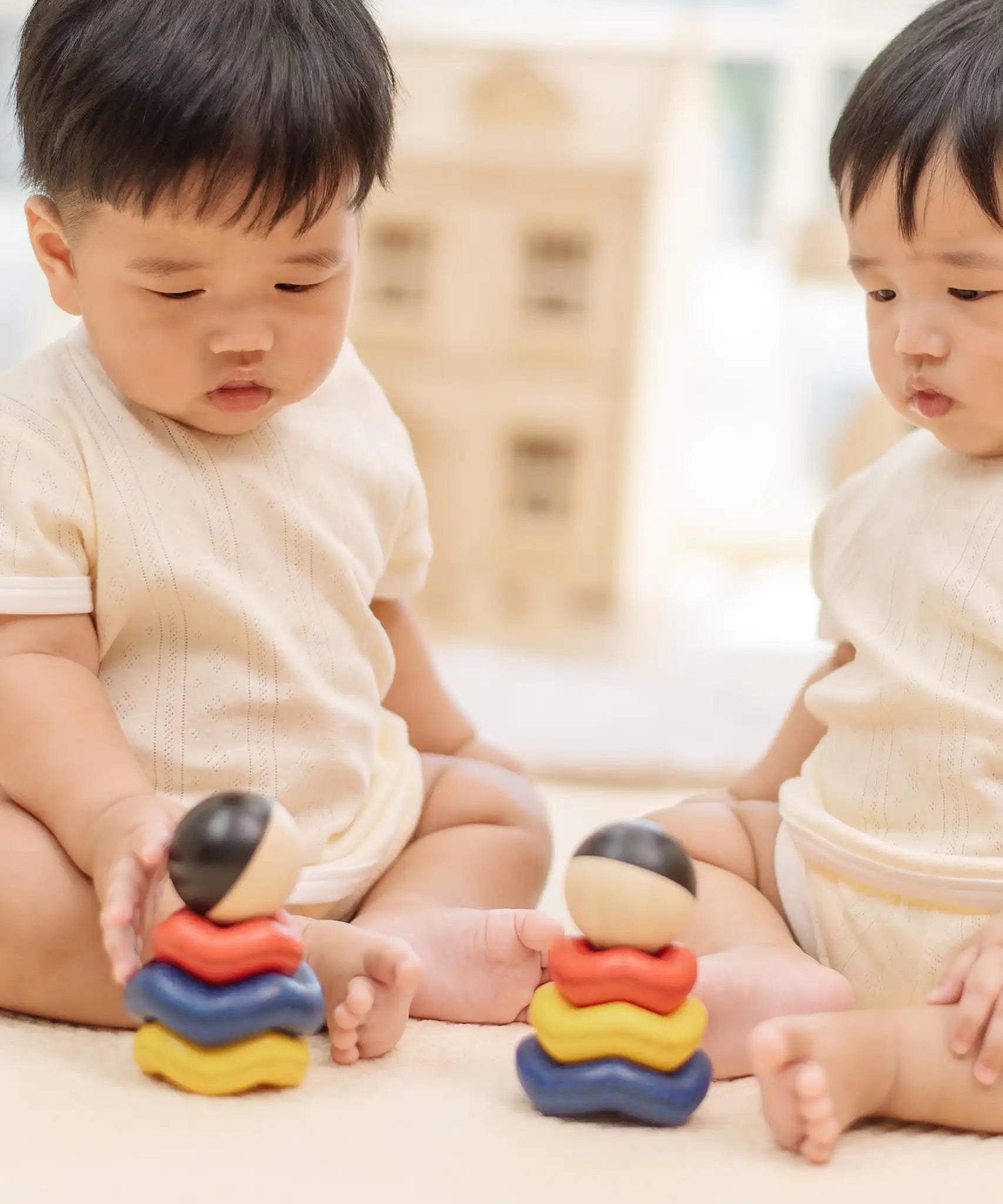 Two babies playing with two of the Baby playing with the PlanToys ball and wave stacker wooden baby stacking toys.