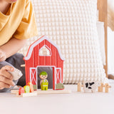 Child playing with the PlanToys barn house small world play set. Red wooden barn, mini veg patch, fences, cow, sheep, hen and farmer figure. 