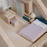 A close up of the bed from the PlanToys Bedroom Dolls House Furniture set placed in a room in a wooden dolls house. 