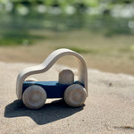 Close up of the Plan Toys kids eco-friendly vroom lorry toy on some sand in front of some green sea water