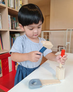 Boy stood at a table playing with the Plan Toys wooden chisel and mallet toy