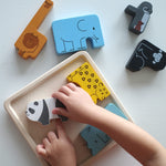Close up of a childs hands moving the pieces from the Plan Toys plastic free animal puzzle game on a white table