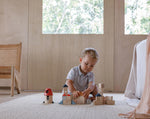 A child playing with the PlanToys Creative Blocks in the Orchard colour way. The child is sitting on a rug.  