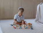 A child playing with the PlanToys Creative Blocks in the Orchard colour way. The child is sitting on a rug.  