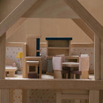 A side on view of the pieces from the PlanToys Dining Room Dolls House Furniture set set up in a wooden dolls house. 
