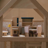 A side on view of the pieces from the PlanToys Dining Room Dolls House Furniture set set up in a wooden dolls house. 

