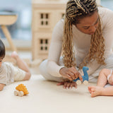 Two children and an adult playing with the PlanToys Dino wooden Car toys. A blue coloured diplodocus, a yellow stegosaurus and red coloured t-rex dinosaur figures on wheels. PlanToys range of toys are made from sustainably sourced rubberwood, we're proud stockists of PlanToys here at Babipur. 