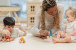 Two children and an adult playing with the PlanToys Dino wooden Car toys. A blue coloured diplodocus, a yellow stegosaurus and red coloured t-rex dinosaur figures on wheels. PlanToys range of toys are made from sustainably sourced rubberwood, we're proud stockists of PlanToys here at Babipur. 