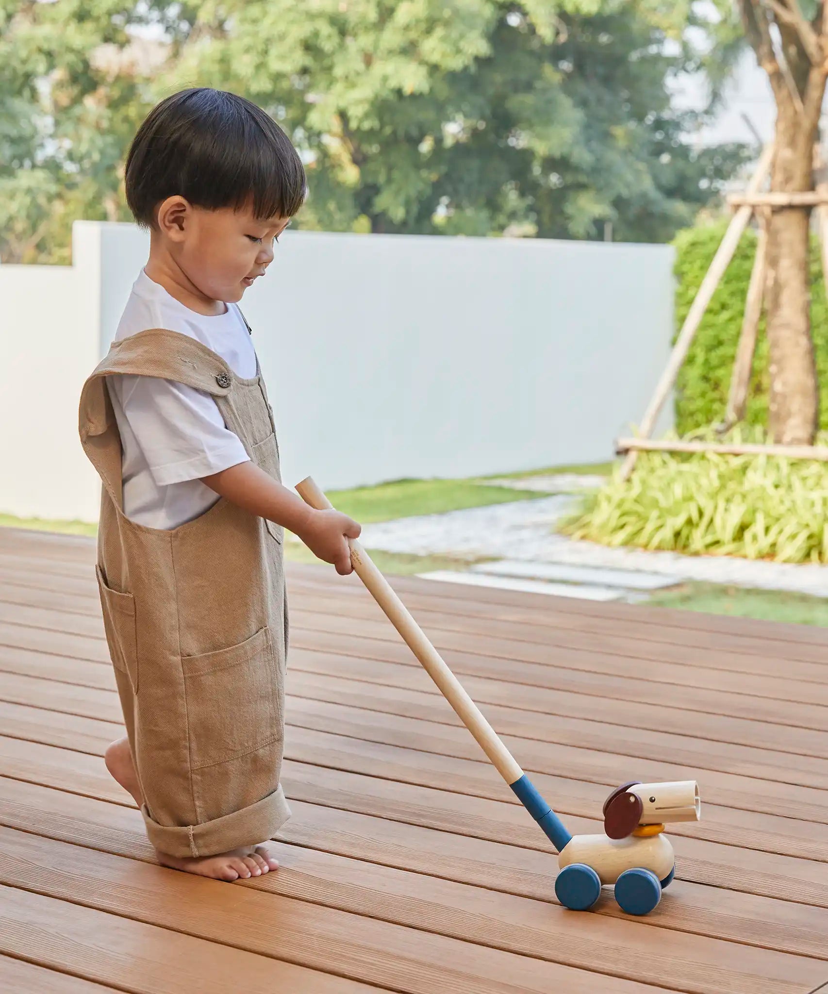 Child pushing the PlanToys push and pull puppy wooden toy along with the stick attachment.