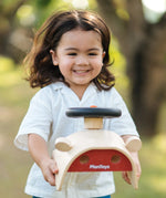 Child carrying the PlanToys Driving Console wooden toy in their hands.