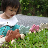 Girl crouched down looking at a line of Plan Toys plastic free wooden rolling bunny toys on some green grass