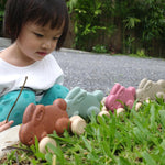 Girl crouched down looking at the Plan Toys plastic free wooden rolling bunnies lined up on some green grass