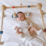 A baby laying underneath the PlanToys Play Gym Orchard. 