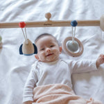 A baby laying underneath the PlanToys Play Gym Orchard .