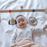 A baby laying underneath the PlanToys Play Gym Orchard .