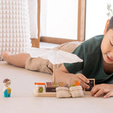 Child playing with the PlanToys Farmer's Market wooden toy playset placing the advert board besides the market stall. 