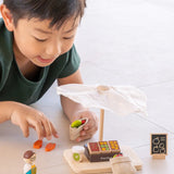Child playing with the PlanToys Farmer's Market wooden toy playset. Child is placing play food produce into the mini jute bags.