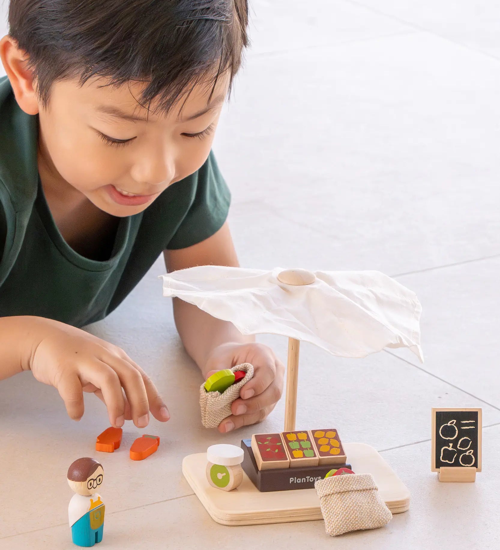 Child playing with the PlanToys Farmer's Market wooden toy playset. Child is placing play food produce into the mini jute bags.
