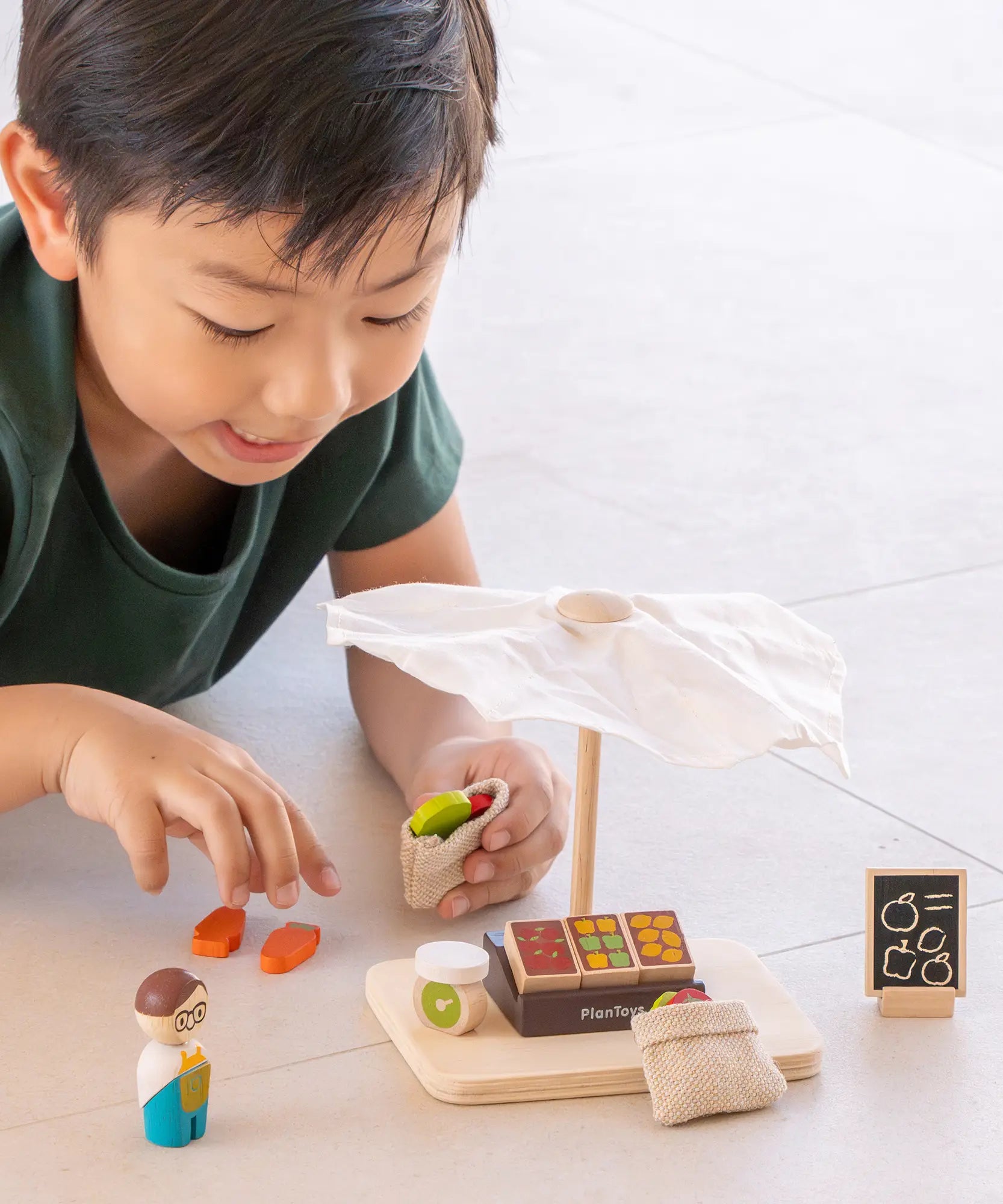 Child playing with the PlanToys Farmer's Market wooden toy playset. Child is placing play food produce into the mini jute bags.