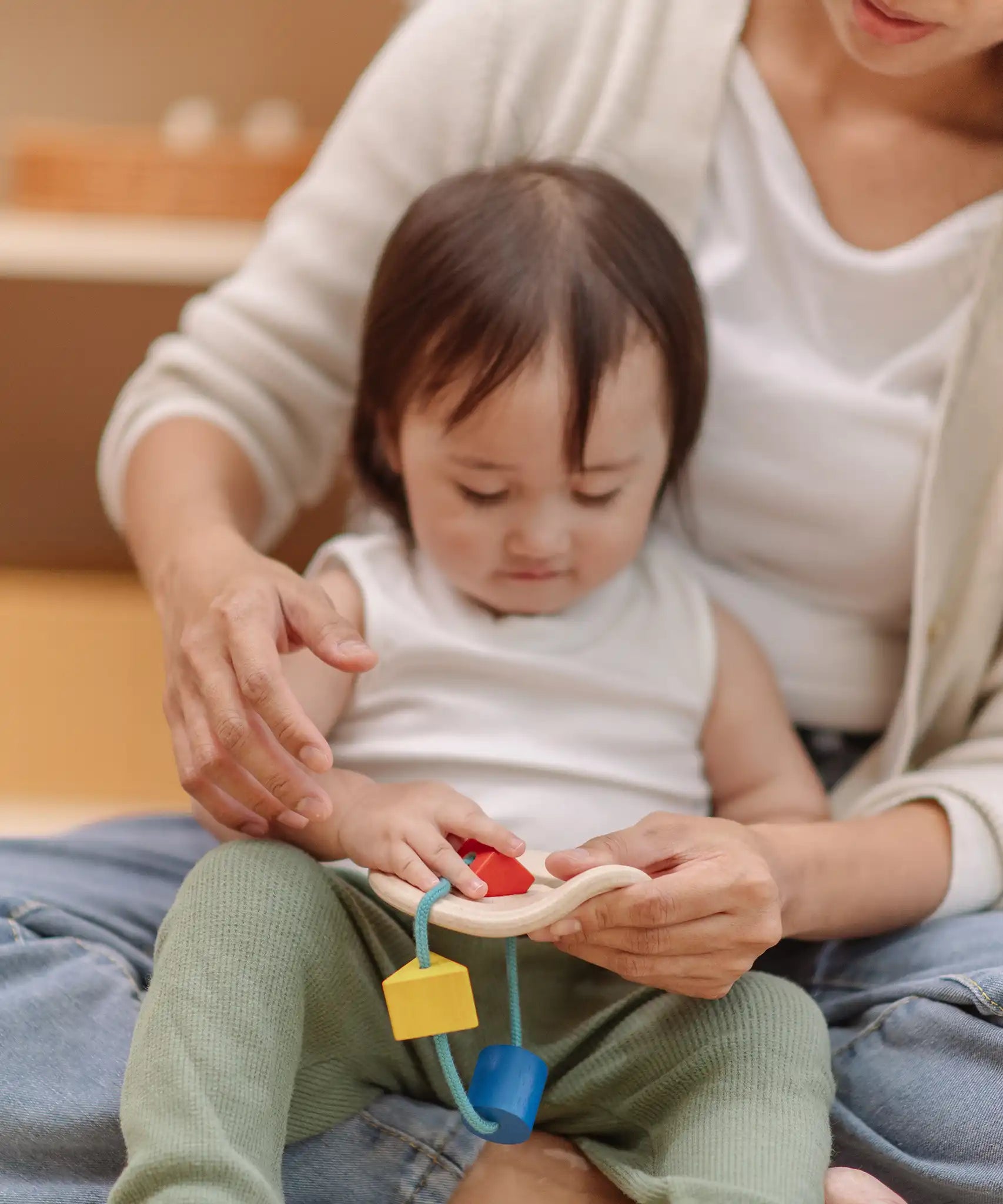 Child playing the PlanToys first shape sorter wooden baby toy pushing the red square piece through the slots on the frame.