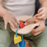 Close up of a child's hand playing with the PlanToys first shape sorter wooden baby toy pushing the red square piece through the slots on the frame.