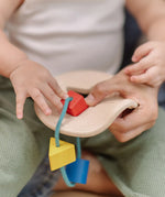 Close up of a child's hand playing with the PlanToys first shape sorter wooden baby toy pushing the red square piece through the slots on the frame.