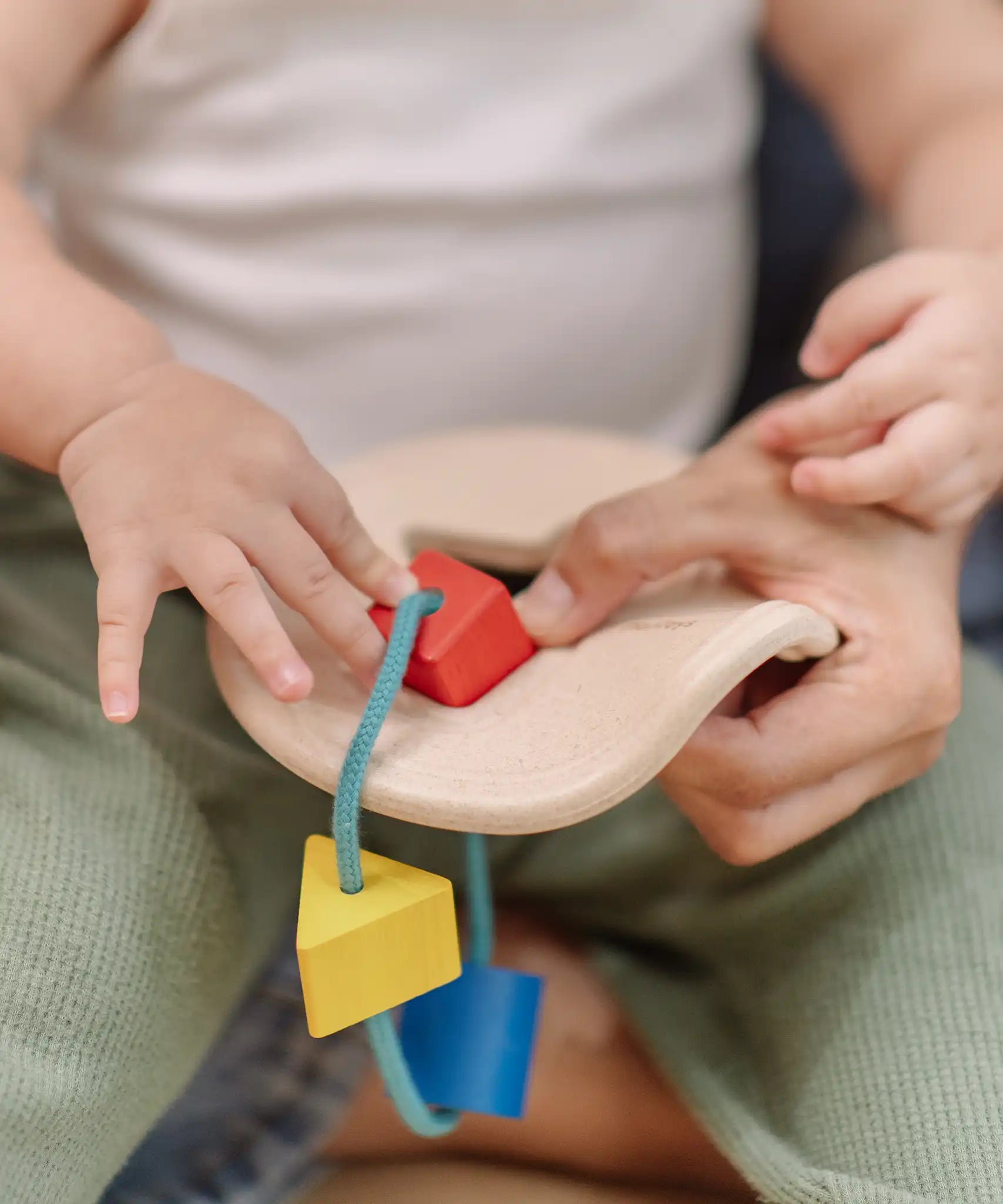 Close up of a child's hand playing with the PlanToys first shape sorter wooden baby toy pushing the red square piece through the slots on the frame.