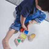 A child sitting on a floor playing with the PlanToys Geo Matching Blocks. 