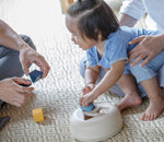 A toddler playing with the PlanToys Geometric Sorting toy, an adult is playing with them. 