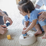 A toddler playing with the PlanToys Geometric Sorting toy, an adult is playing with them. 