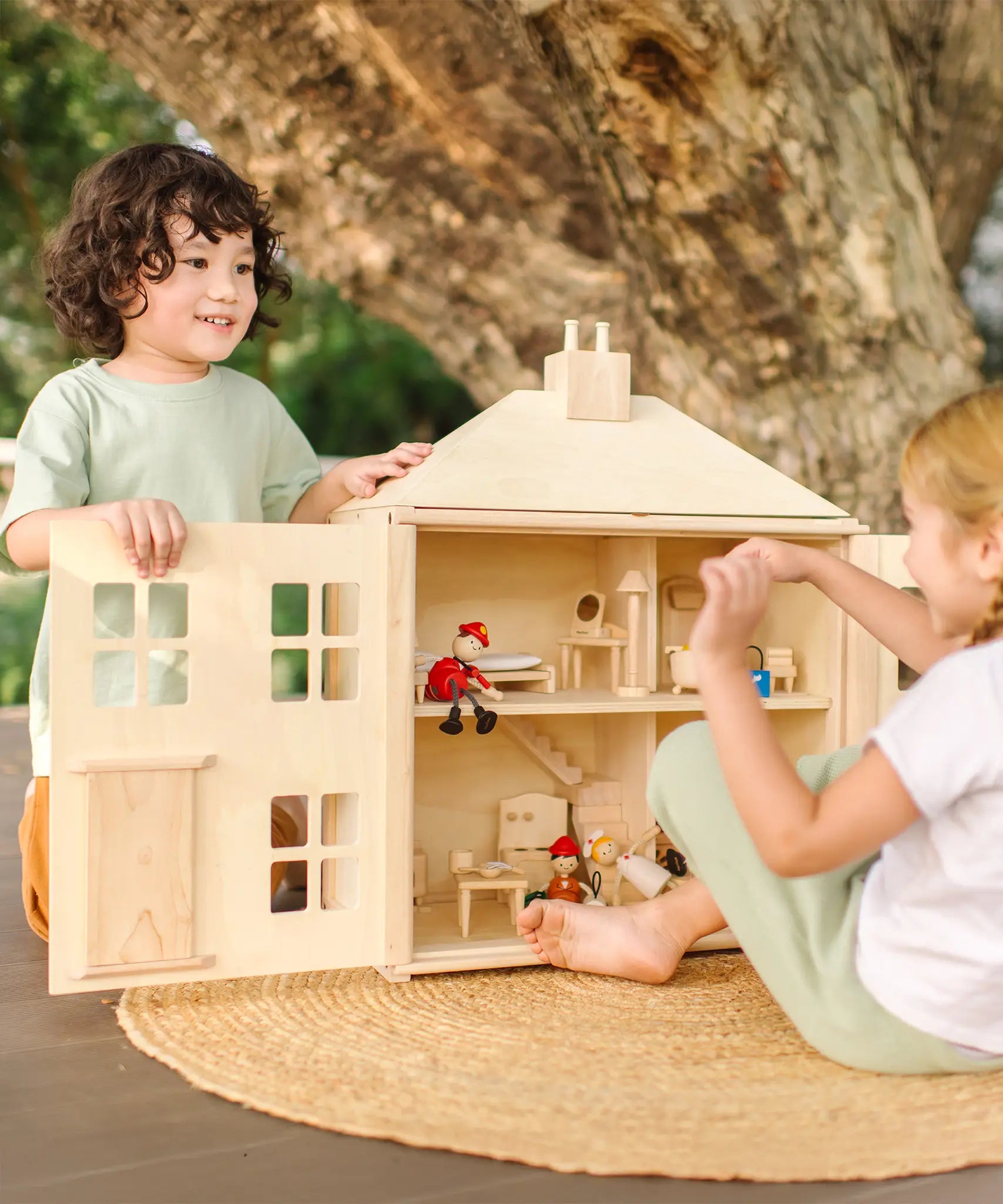 Children playing with the PlanToys wooden Georgian dollhouse children's toy. The house has been filled with dolls house furniture and wooden doll figures.