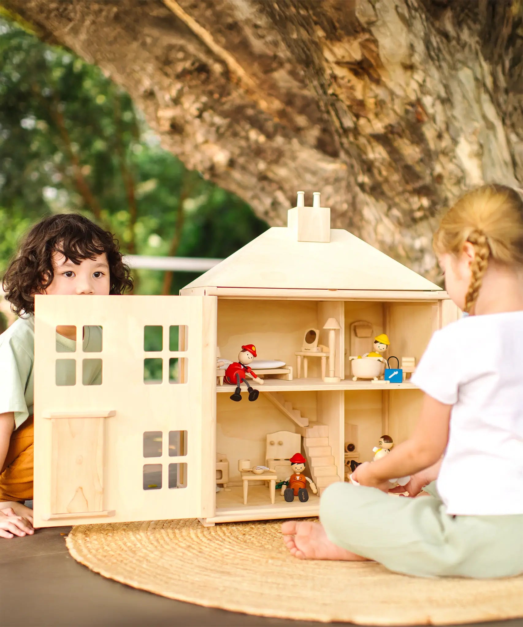 Children playing with the PlanToys wooden Georgian dollhouse children's toy. The house has been filled with dolls house furniture.
