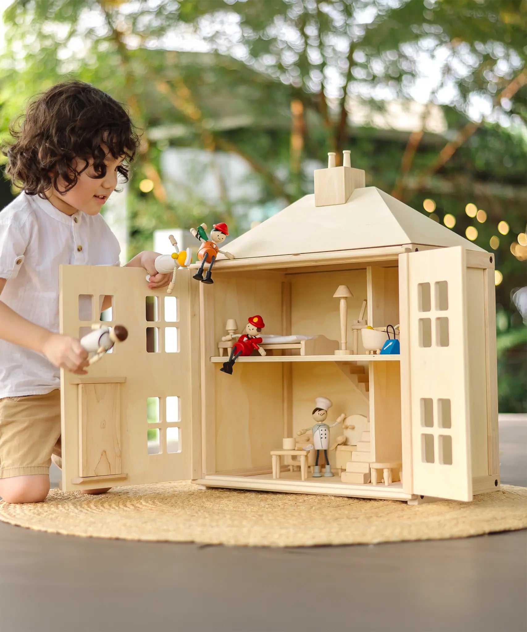 Child playing with the PlanToys wooden Georgian dollhouse children's toy. The house has been filled with dolls house furniture.