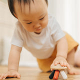 A baby placing their hand on the PlanToys Flexi Jellyfish wooden high contrast baby toy. A wooden top with high contrast, white, greys, black and red flexible wooden pieces for the jellyfish legs. PlanToys range of toys are made from sustainably sourced rubberwood, we're proud stockists of PlanToys here at Babipur.  