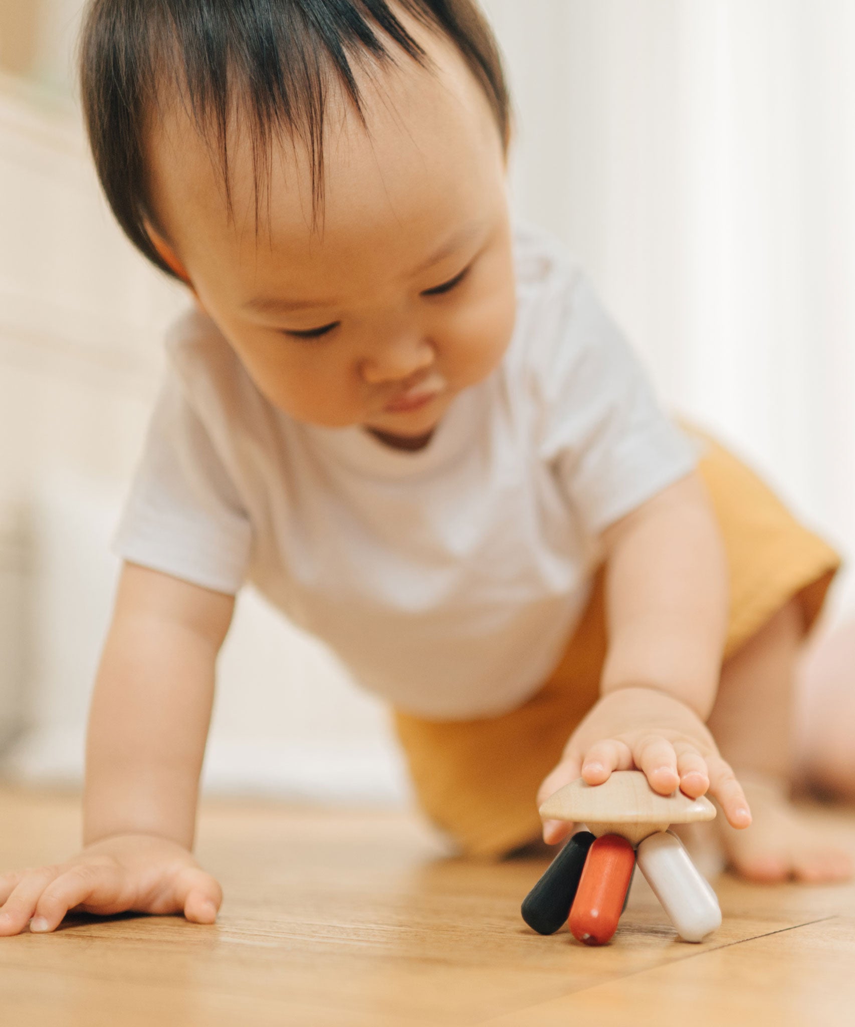 A baby placing their hand on the PlanToys Flexi Jellyfish wooden high contrast baby toy. A wooden top with high contrast, white, greys, black and red flexible wooden pieces for the jellyfish legs. PlanToys range of toys are made from sustainably sourced rubberwood, we're proud stockists of PlanToys here at Babipur.  