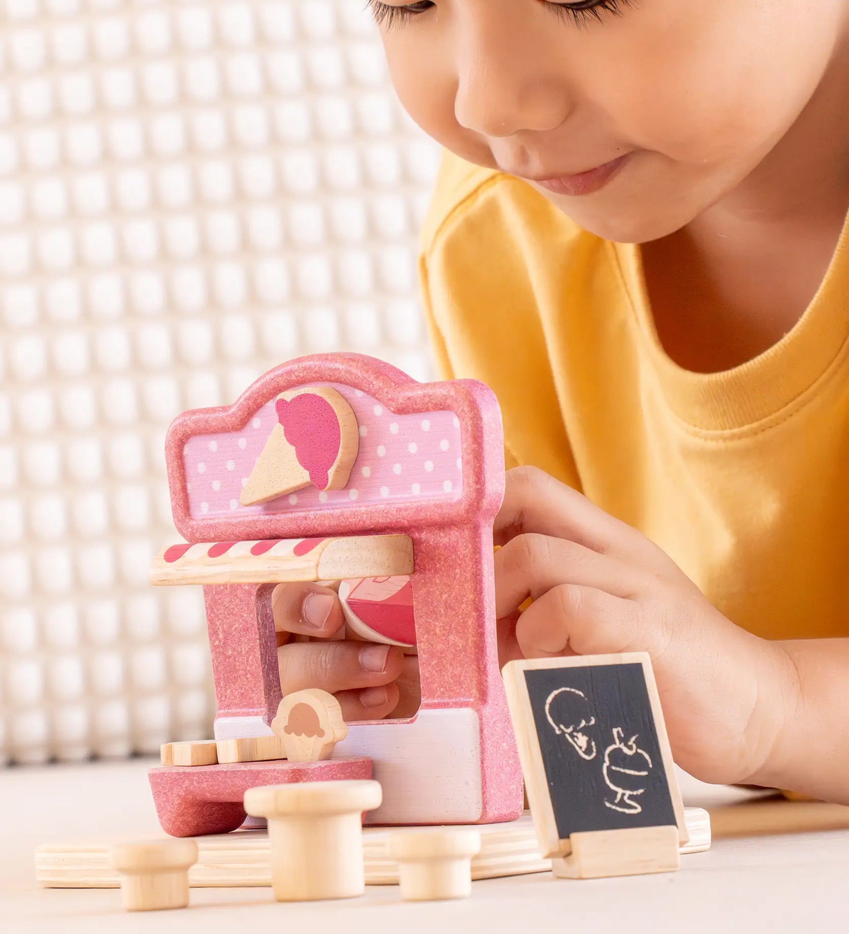Child playing with the PlanToys ice cream shop wooden toy playset, holding the wooden worker figure.
