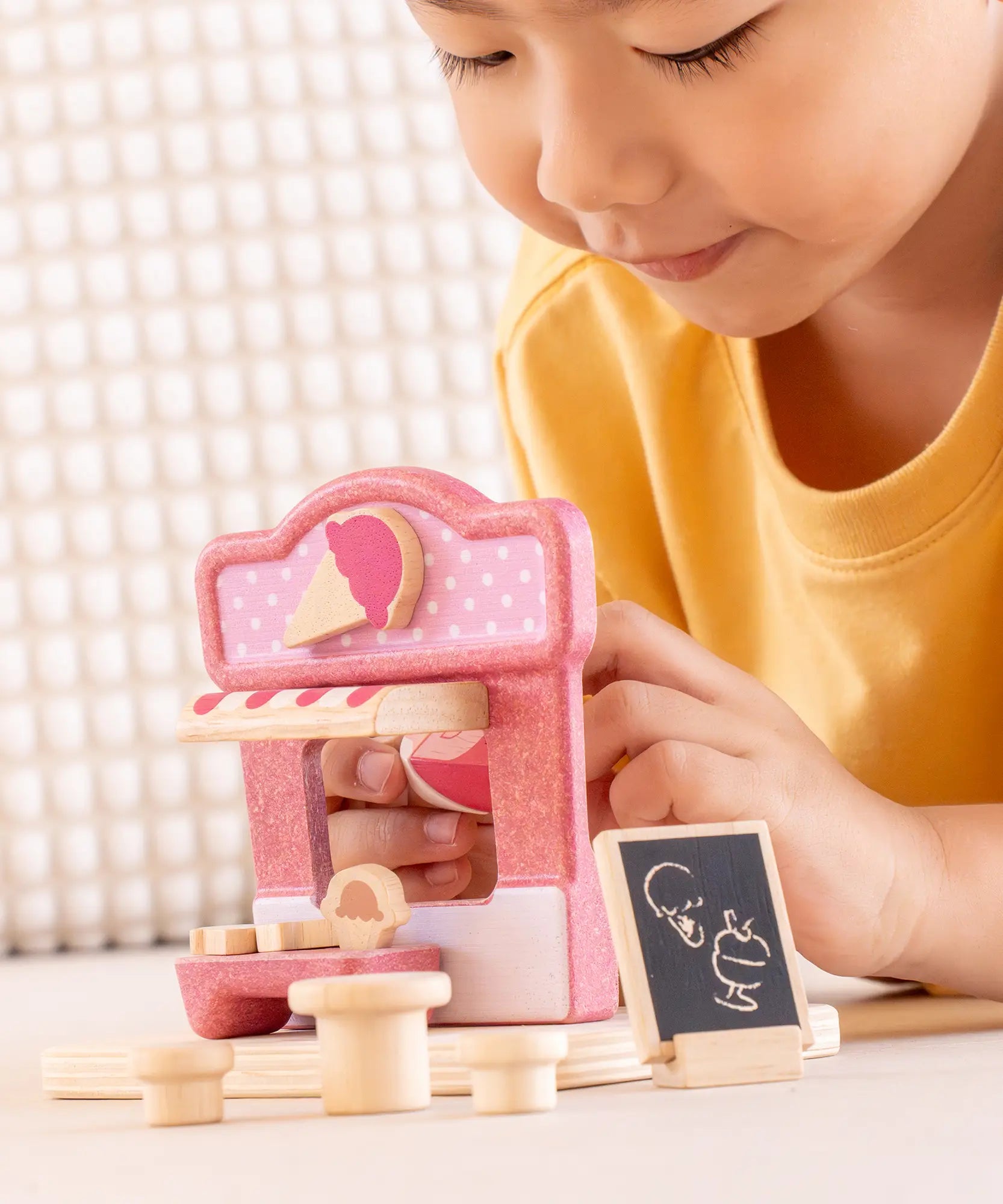Child playing with the PlanToys ice cream shop wooden toy playset, holding the wooden worker figure.