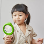 A child holding a PlanToys Leaf Magnifier toy in their hand.