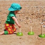 A child on the beach playing with the PlanToys Meadow Ring Toss. 
