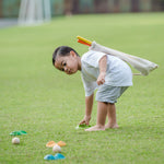 A child playing with a the PlanToys Mini Golf Set outside on grass. He is picking up one of the green wooden hole. 