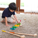 A child sitting on a rug setting up the pieces from the PlanToys mini wooden golf set.  
